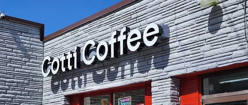 Cotti Coffee storefront lettering in white on a grey stone-effect wall above red window frames