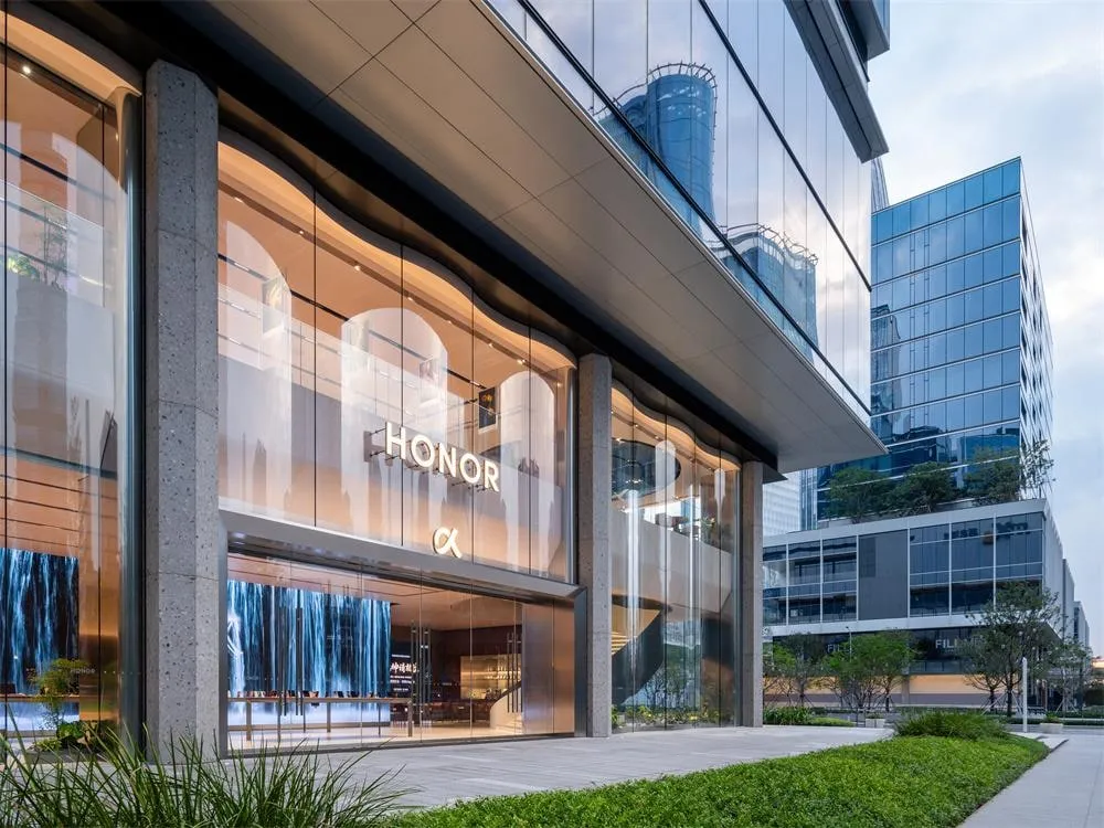 Honor flagship store at dusk, with a wave-edged glass facade, the HONOR sign and a video wall inside
